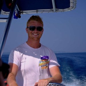 Man in sunglasses steering a boat on a sunny day.