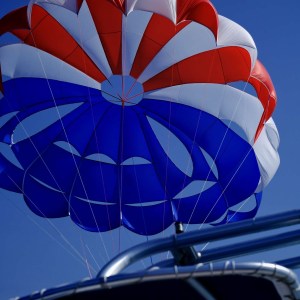 Red, white, and blue parasail against a clear blue sky.