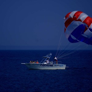 Boat with parasailers in open sea against a clear blue sky.