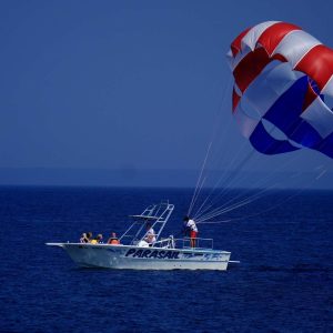 Boat with people parasailing using a red, white, and blue parachute over the ocean.