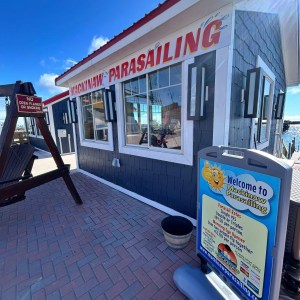 Building with 'Mackinaw Parasailing' sign, blue sky, and a wooden swing.