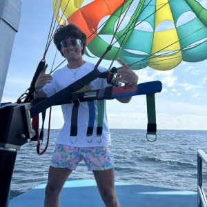 Person in colorful attire ready for parasailing on a boat, blue sky and ocean in background.