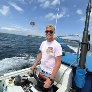 Smiling person steering a boat on the ocean under a partly cloudy sky.