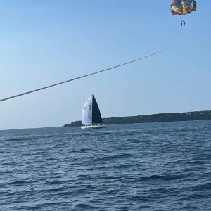 Parasailing person above ocean, boat with sail in background.