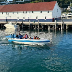 Small boat with people on water near dock and white building with red roof.