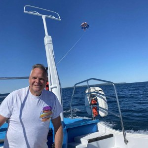 Man on a boat with parasail in the background over the ocean under a clear blue sky.