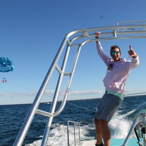 Person giving thumbs up on boat with parasailer in the background over the sea.
