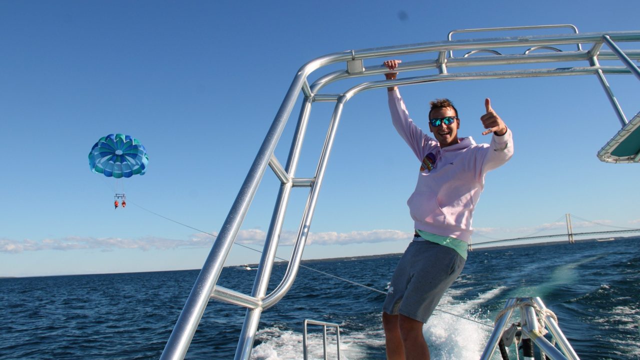 Person giving thumbs up on boat with parasailer in the background over the sea.
