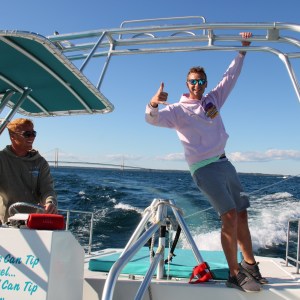 Two people on a boat; one steering, the other posing with a thumbs-up.
