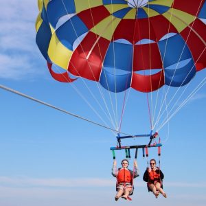 Two people parasailing over the ocean with a multicolored parachute.