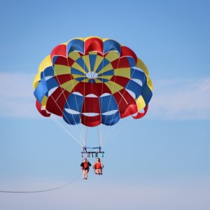 Two people parasailing with a colorful parachute against a clear blue sky.