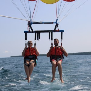 Two people parasailing over the ocean, wearing life jackets.