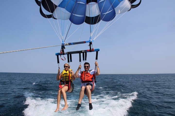 Two people parasailing over the ocean, wearing life jackets.