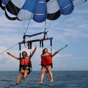 Two people parasailing over the ocean in life vests, smiling.