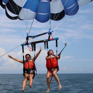 Two people parasailing over the ocean with blue sky and clouds.
