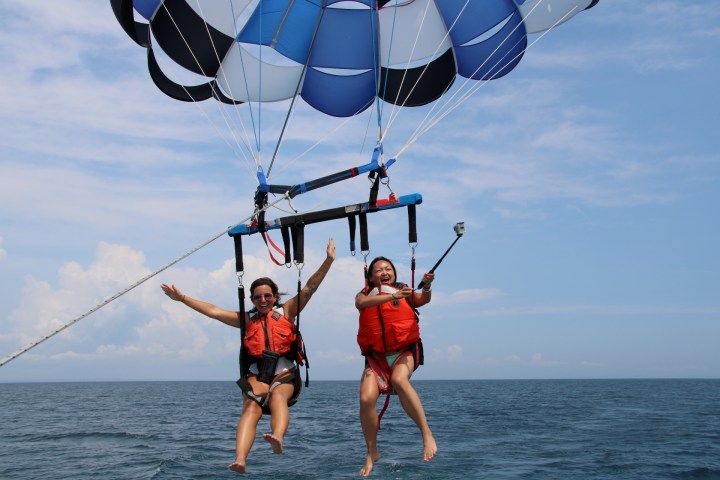 Two people parasailing over the ocean with blue sky and clouds.