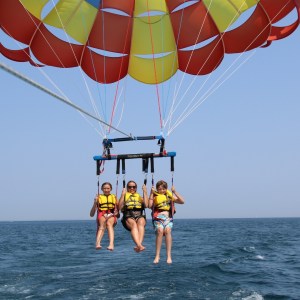 Three people parasailing over the ocean with a colorful parachute.