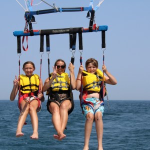 Three people parasailing over the ocean, wearing yellow life jackets.