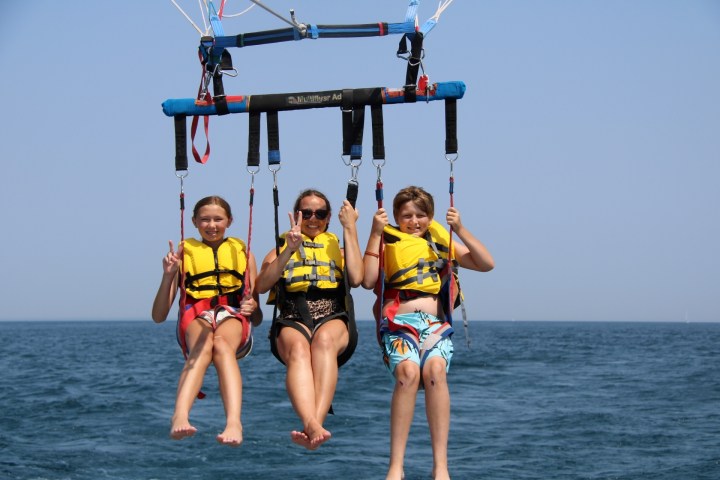 Three people parasailing over the ocean, wearing yellow life jackets.