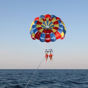 Two people parasailing over the ocean with a colorful parachute.