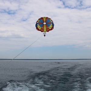 Person parasailing over open water with colorful parachute.