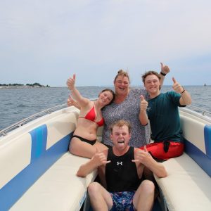 Four people on boat, smiling and giving thumbs up on open water.