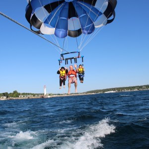 Three people parasailing over water with a lighthouse in the background.