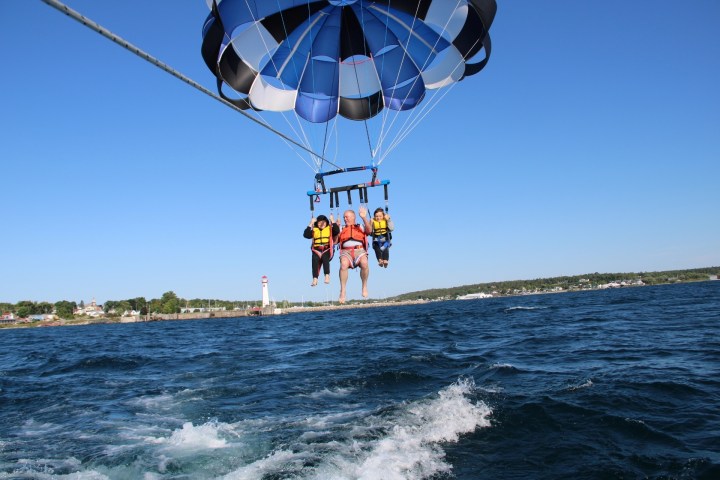 Three people parasailing over water with a lighthouse in the background.
