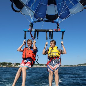 Two people parasailing over the ocean, wearing life jackets and harnesses.