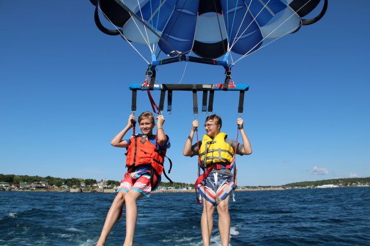 Two people parasailing over the ocean, wearing life jackets and harnesses.