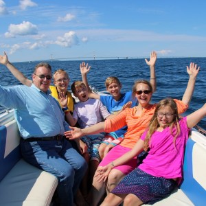 Smiling family with raised arms on a boat in the ocean.