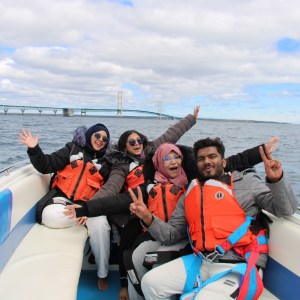 Four people in life jackets smiling and posing on a boat with a bridge in the background.