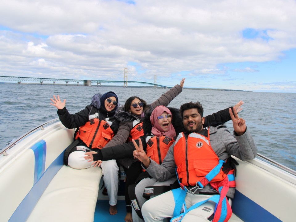 Four people in life jackets smiling and posing on a boat with a bridge in the background.